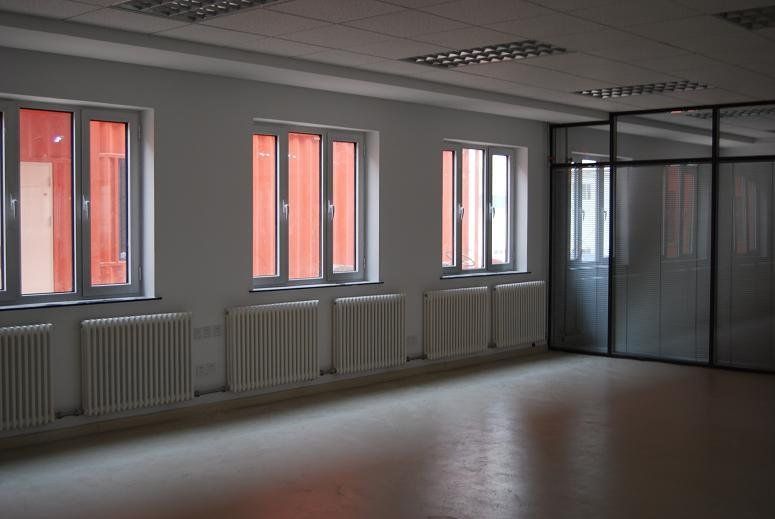 Empty room with windows and radiators, reflecting orange light. Glass-walled room in corner.