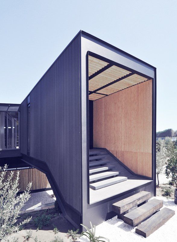 Modern building exterior with angled dark gray walls, light wood interior, and stairs.