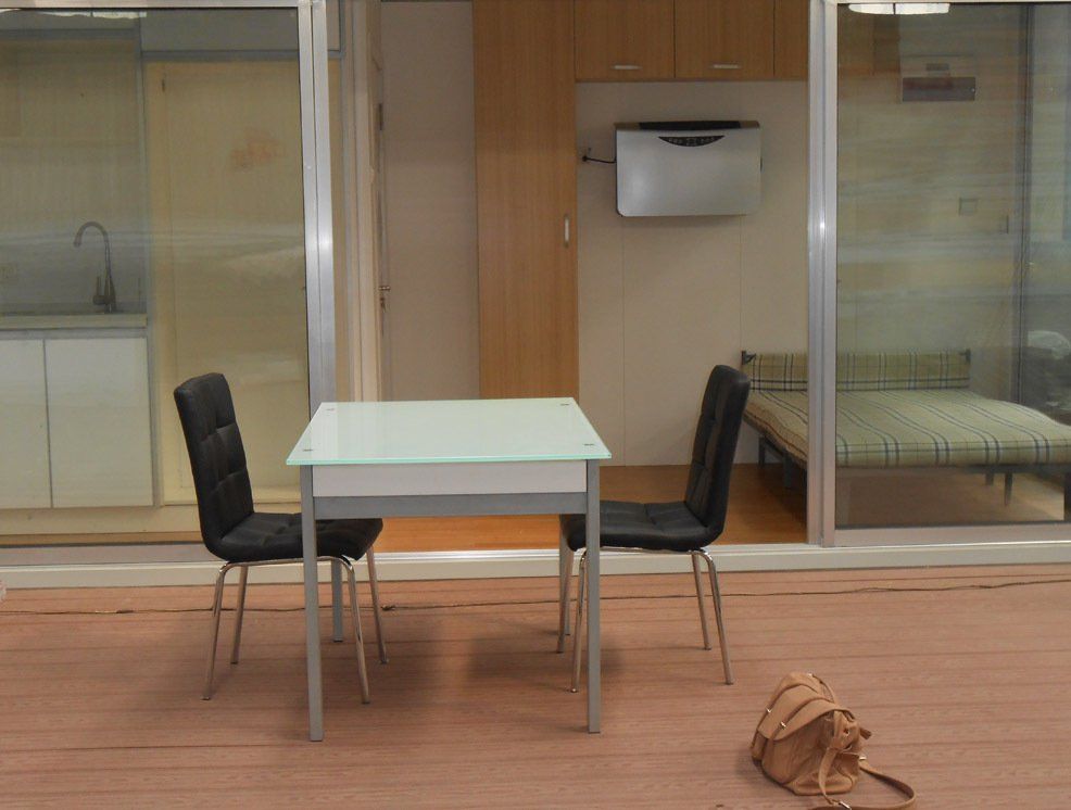 Two black chairs face a table; a purse sits nearby. A room with a bed is visible through a sliding glass door.