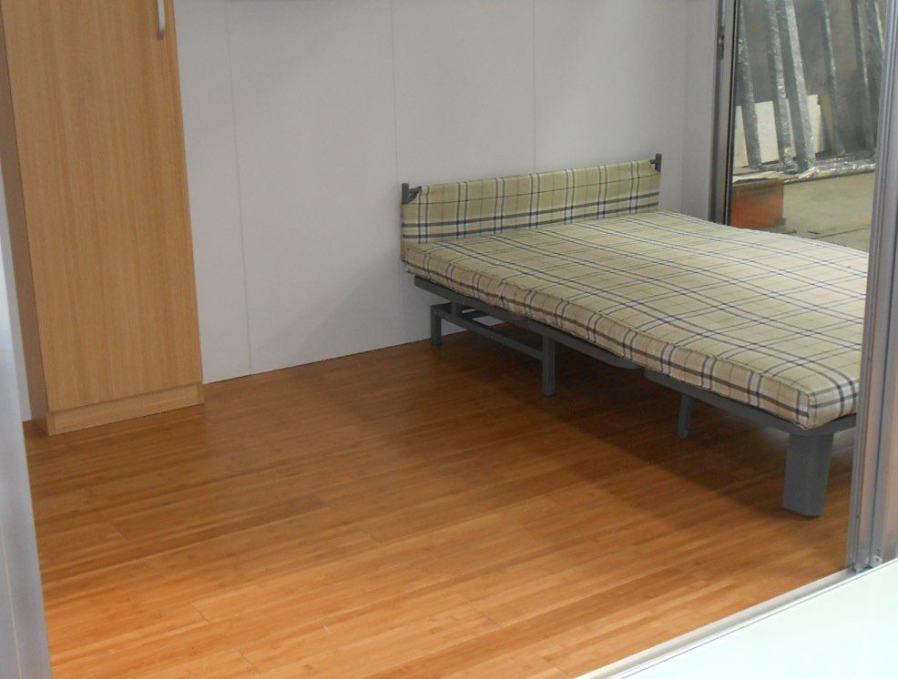 Bedroom with wood floor, metal-framed bed, wardrobe, and window with curtains.