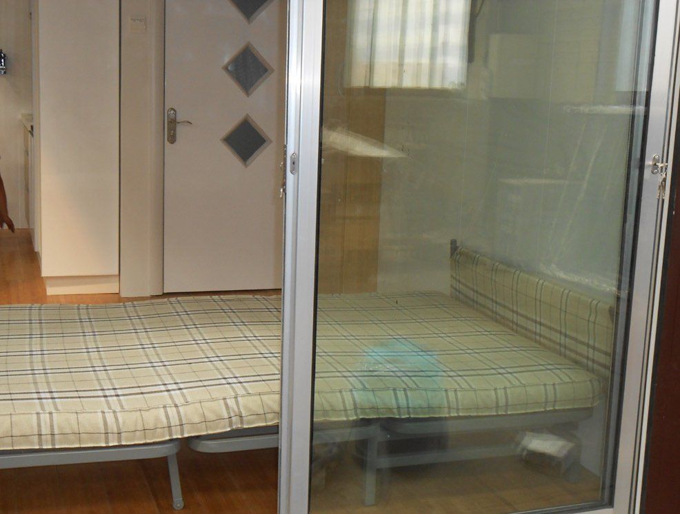 Bedroom with a bed visible through a sliding glass door. Another bed and a white door are in view.