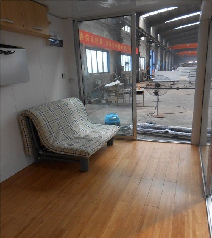A small room with a sofa facing a large window overlooking an industrial area; wooden floor and white walls.