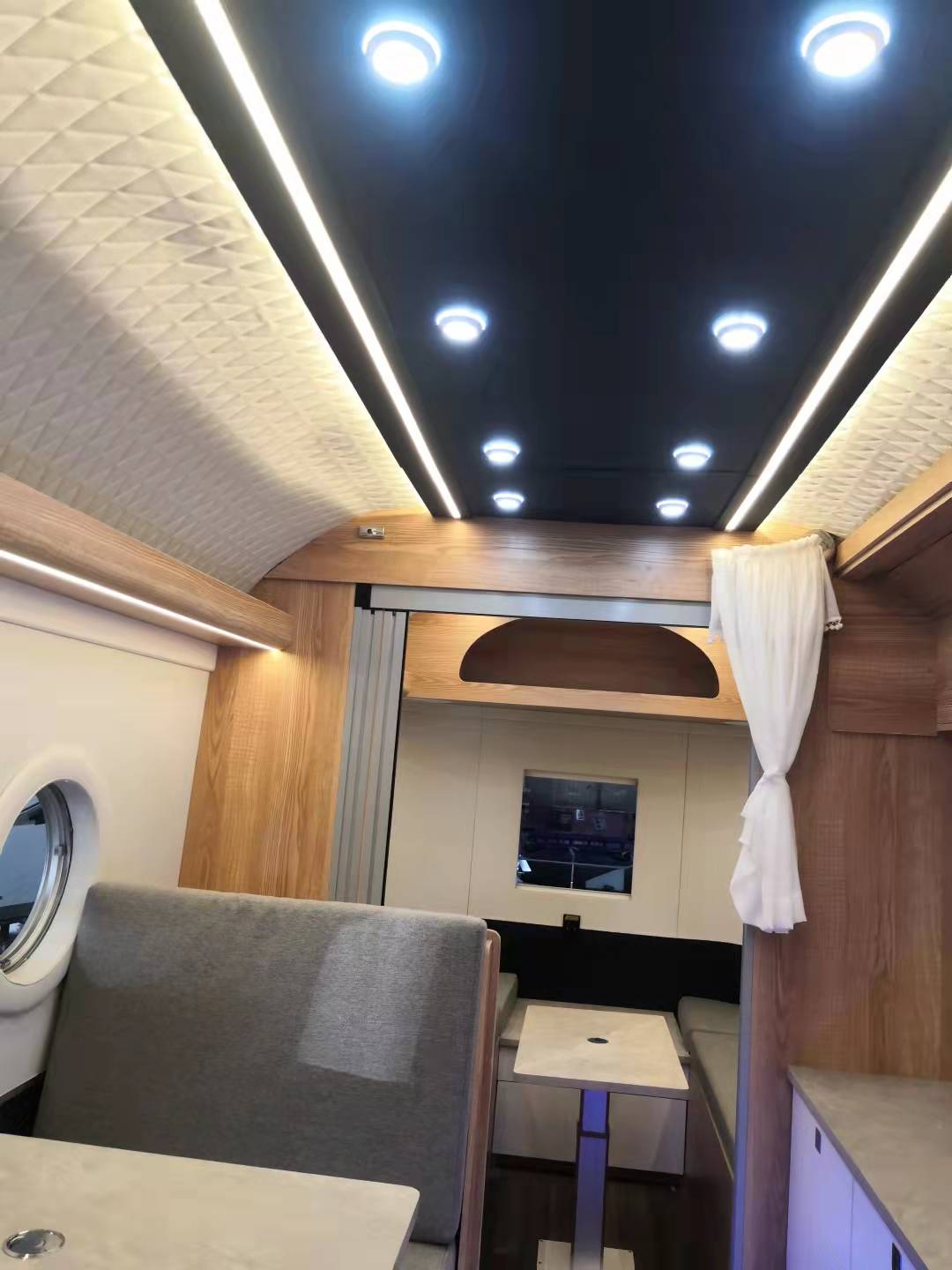 Interior of a camper van with wood paneling, diamond-patterned ceiling, and recessed lighting.