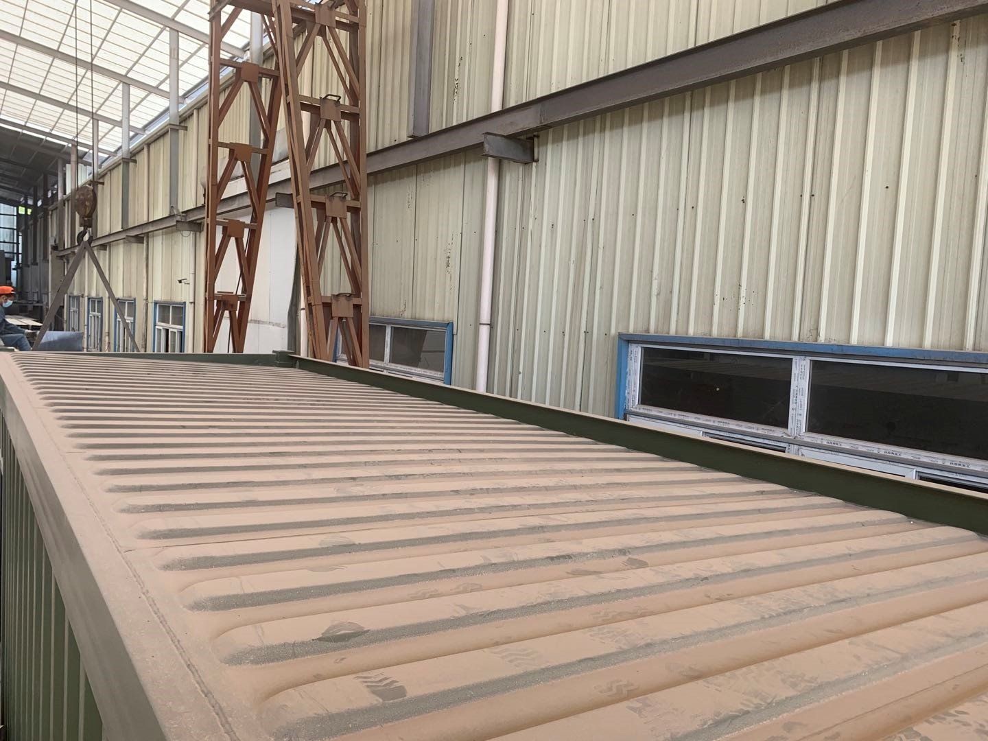 Industrial building exterior with corrugated metal roof and wall, windows, and support structure.