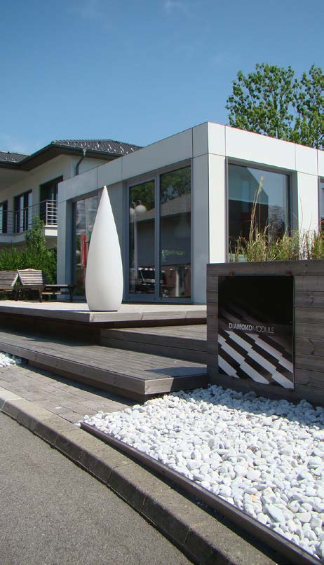 Modern white building with large windows and wooden deck. A white conical sculpture stands in front.