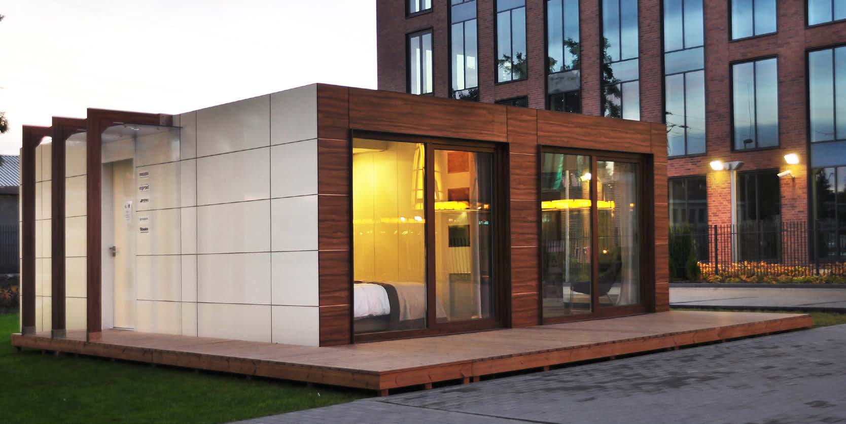 Modern modular home with wood and white paneling, glass doors, and a wooden deck.