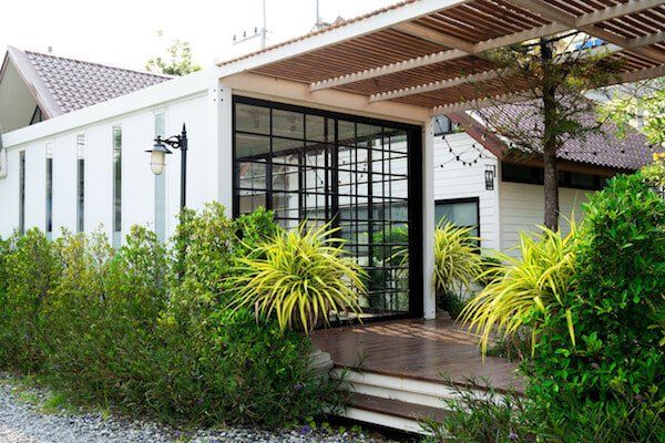 White building with black-framed glass doors, wooden awning, and lush green landscaping.
