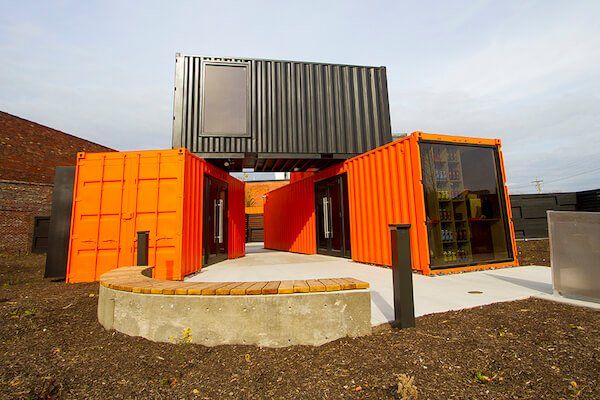 Bright orange and black shipping containers form a modern structure with windows, on a concrete pad.