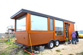 Brown tiny home on wheels with large windows; people standing outside.