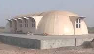Beige dome-shaped building with rectangular windows and a concrete base, in a desert landscape.