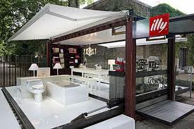 An outdoor Illy coffee shop display with a white interior, including a bathroom, dining area, and coffee bar.