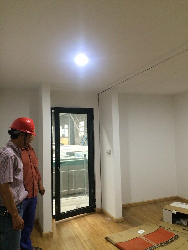 Two people in a room under construction: one in a hard hat, examining a door and flooring.