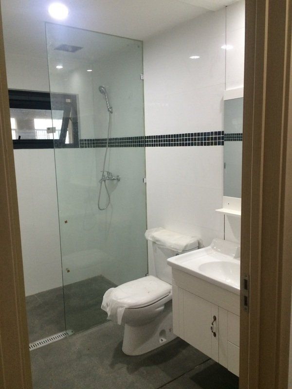 Bathroom with glass shower, white walls, toilet, and sink.
