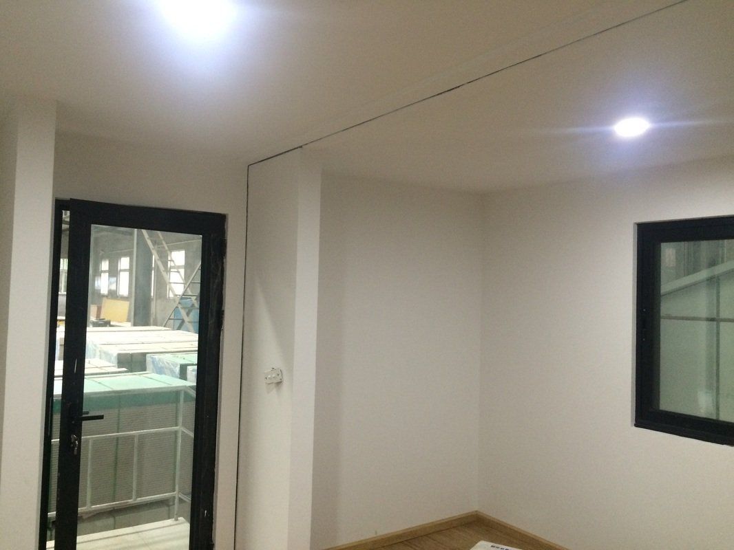 Interior of a white-walled room with a black-framed door and window; a light shines on the ceiling.