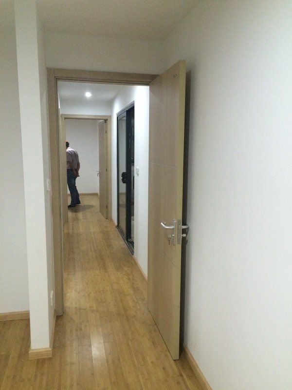 Narrow hallway with wooden floor and several doorways. A person stands in the distance.