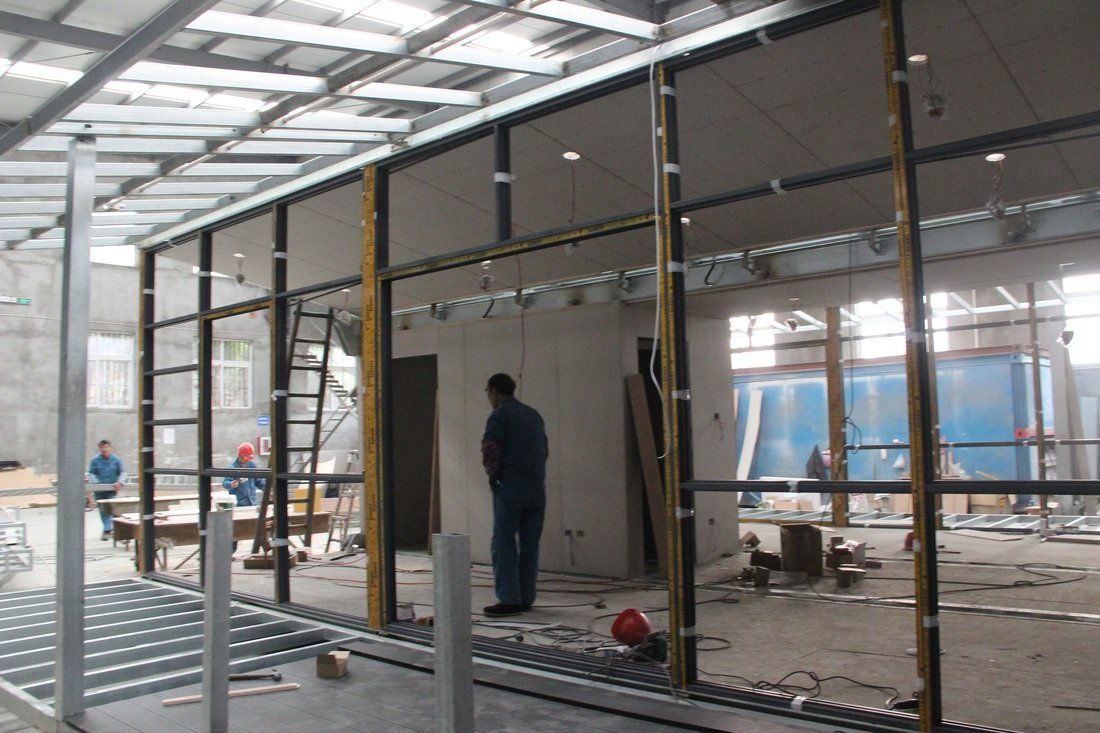 Construction site with glass partition being installed. Workers, tools, and a partial building interior.