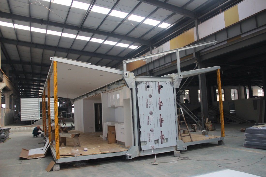 Modular home construction in a large warehouse. Partially built with visible structural elements and open sides.