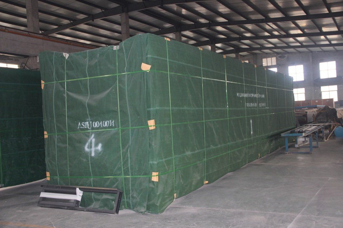 Large, green-wrapped rectangular object in a factory setting, possibly a piece of equipment, with 