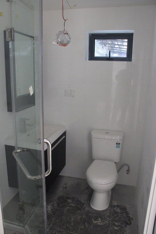 Bathroom with a toilet, sink, mirror, and shower. White walls, dark cabinet, small window.