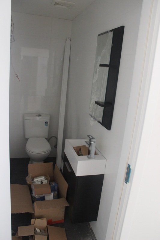 Bathroom with toilet, sink, mirror, and cabinet; construction materials on the floor.