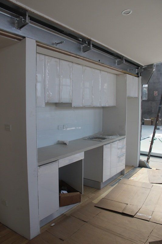 White built-in cabinetry with counter and overhead storage, under construction. Cardboard on floor.