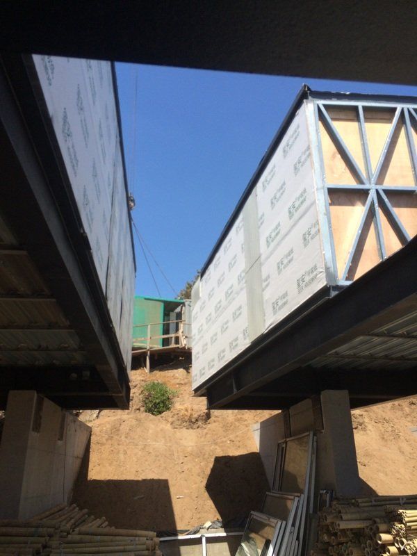 Construction site with two elevated box-like structures. Steel beams and supports are visible, blue sky overhead.