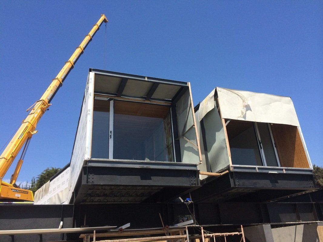 Two modular building sections being lifted by a crane against a blue sky.