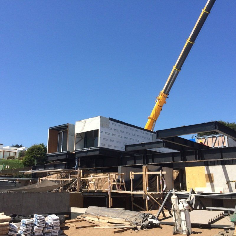 Construction site with crane lifting a modular building section; blue sky.