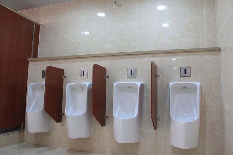 Men's room with four white urinals, brown dividers, and tan tiled walls.
