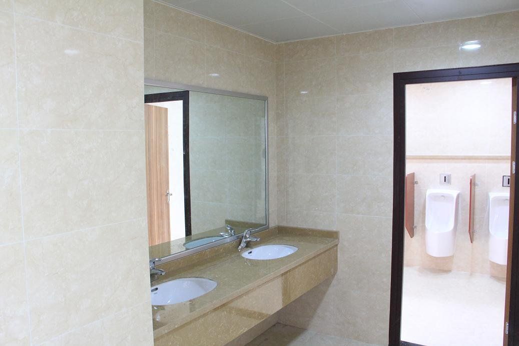 Public restroom with beige tile walls, two sinks, and a doorway to urinals.