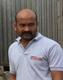 Man wearing a grey polo shirt with a logo, standing outdoors, looking at the camera.