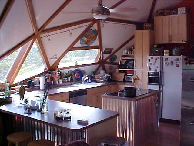 Kitchen in a geodesic dome home, featuring wooden beams, counters, and stainless steel accents.