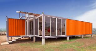 Orange shipping container home with large glass windows and steps, set in a field.