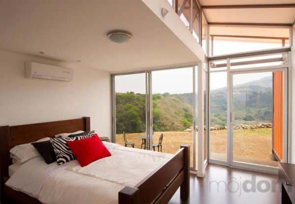 Bedroom with large windows overlooking a scenic landscape. Bed has red, black, and zebra print pillows.