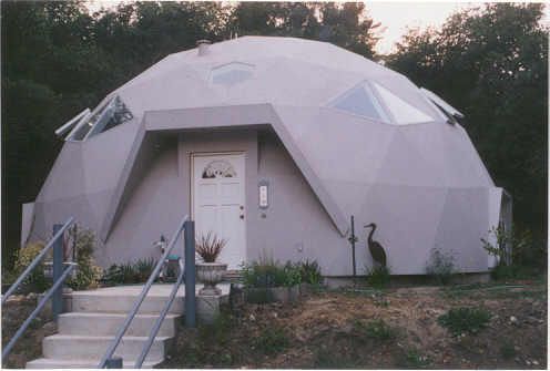 Gray geodesic dome house with white door and triangular windows; steps lead to entrance.