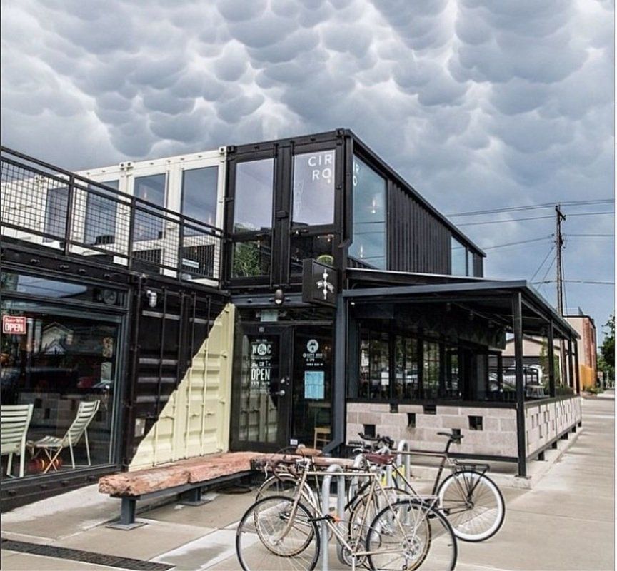A restaurant constructed from shipping containers with bikes parked outside; dramatic, textured clouds overhead.