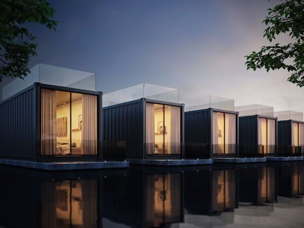 Row of dark, modern cabins on water, lit from within, with glass doors and rooftop decks.