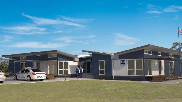 Blue and white modular buildings with flat roofs, flagpole, and parked cars on a grassy area.