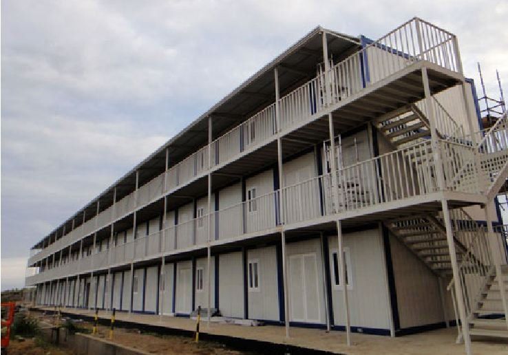 Three-story modular building with white walls, balconies, and exterior stairs under a cloudy sky.
