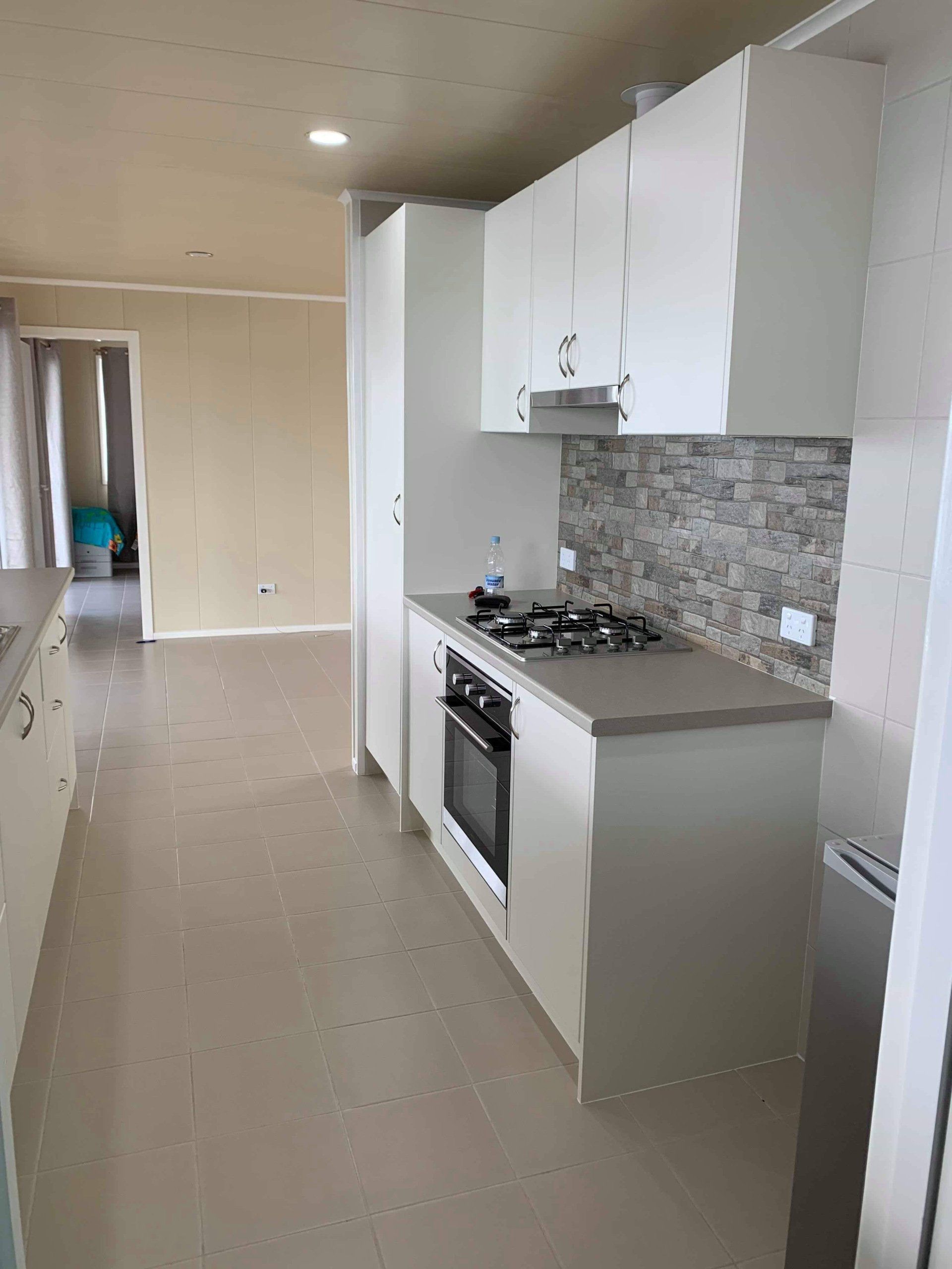 Modern white kitchen with light countertops, stove, and cabinets. Light-colored walls and flooring.
