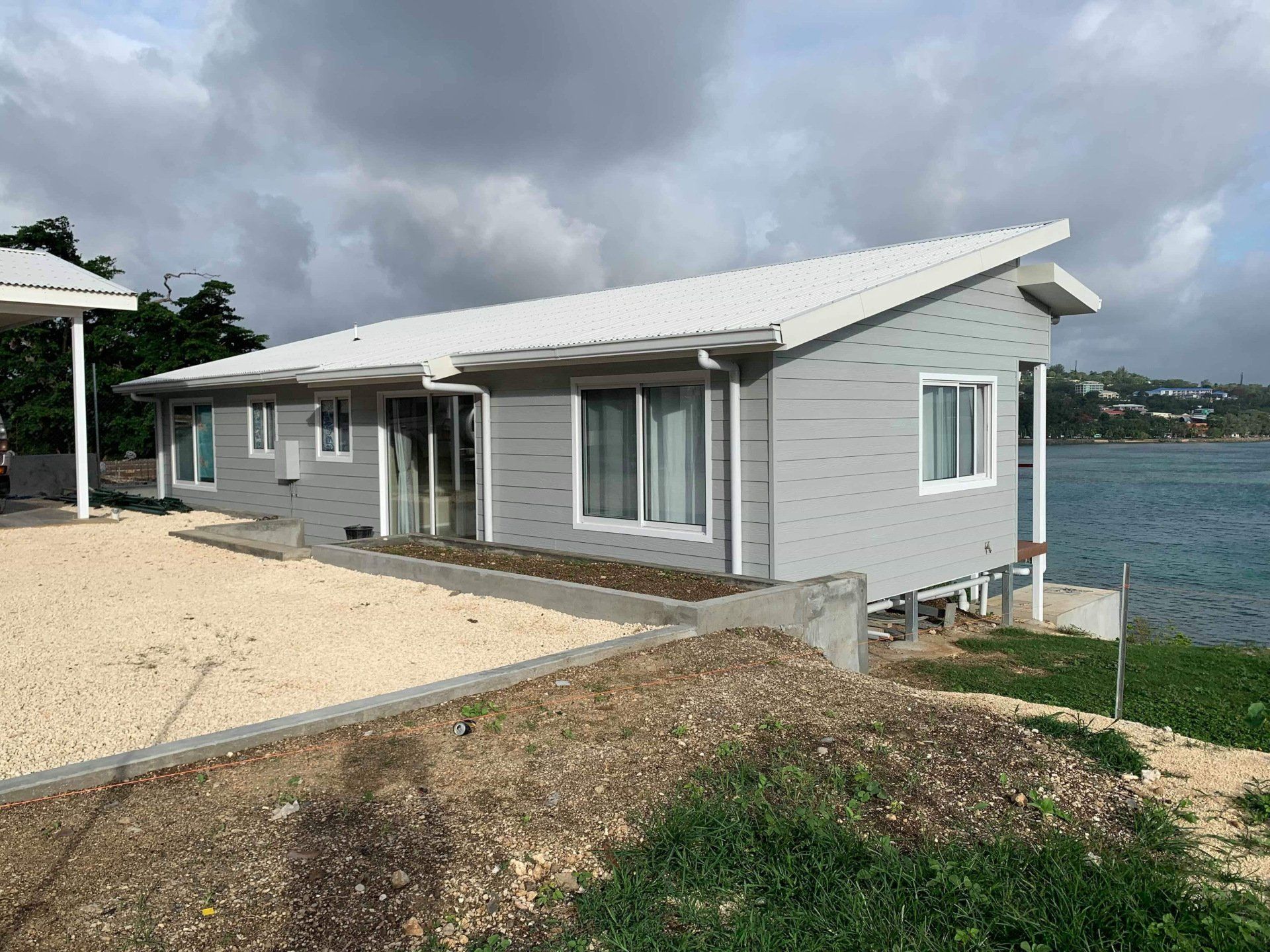 Gray house with white trim and roof near water, cloudy sky overhead.