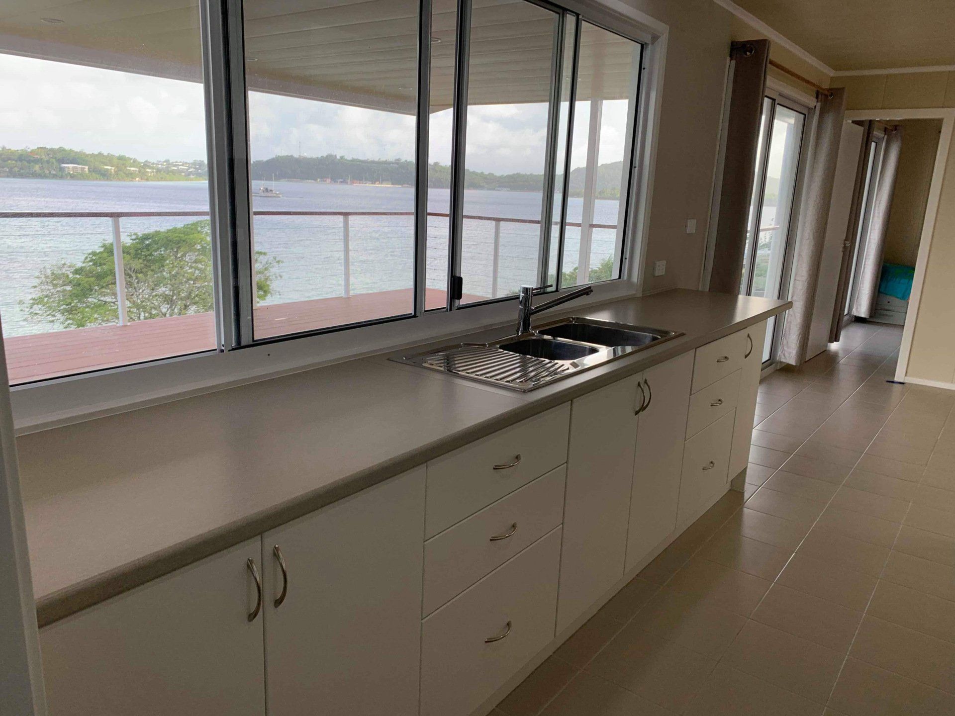Kitchen with white cabinets, stainless steel sink, large windows overlooking water.
