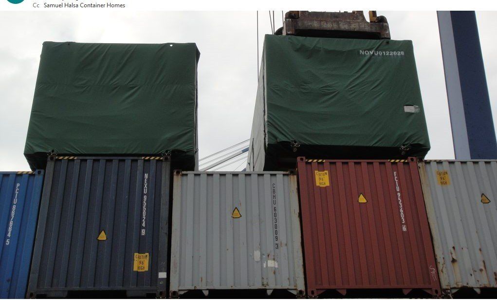 Shipping containers stacked; two covered with green tarps.