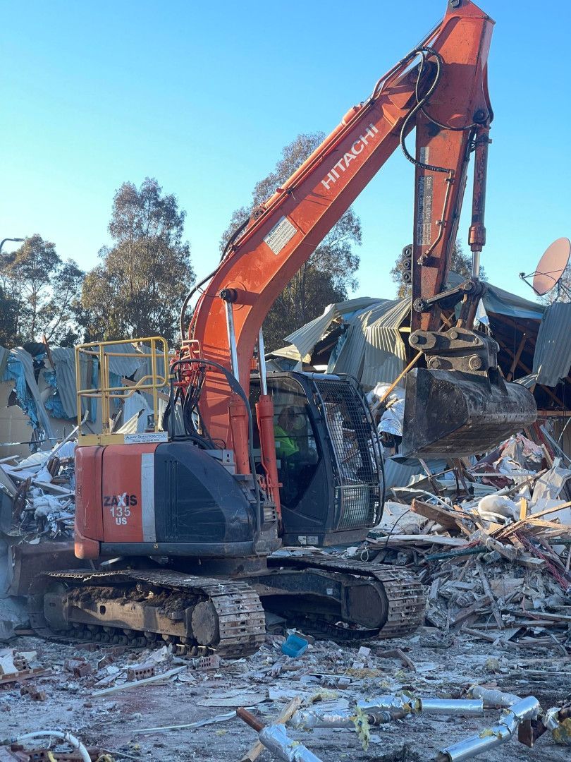 A Orange Excavator Is Demolishing a Brick Building — Albury Demolitions in Lavington, NSW