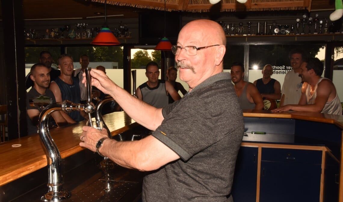 Iemand tapt bier uit een tapkraan in een bar, met klanten op de achtergrond.