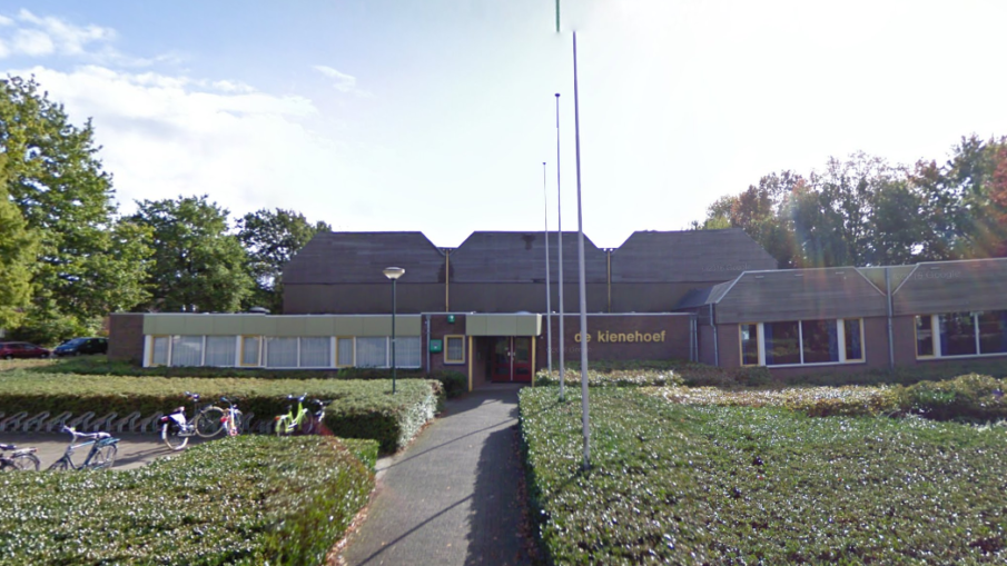 Een laag bakstenen gebouw met een centrale ingang onder een zonnige hemel