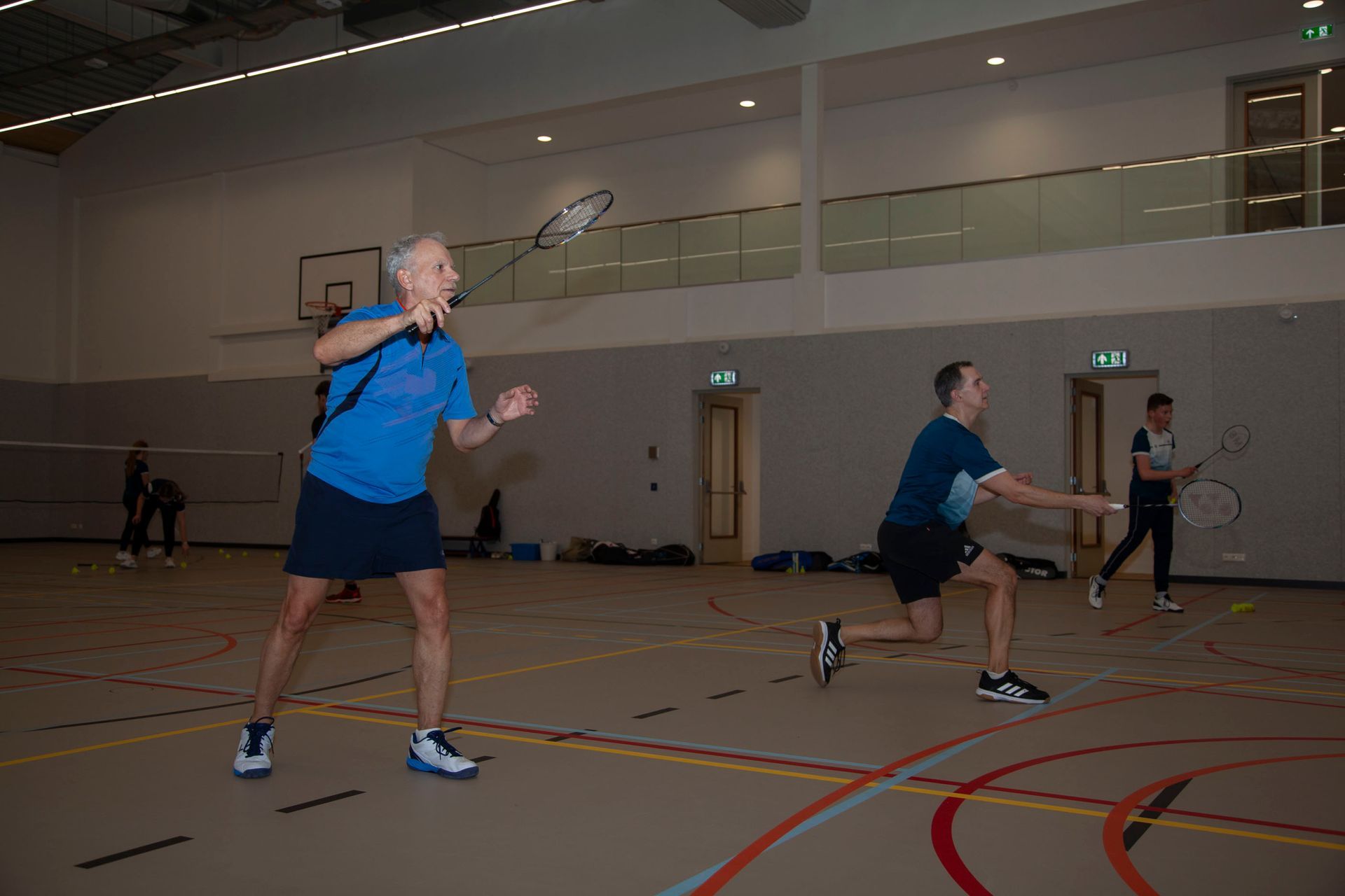 Drie mensen spelen badminton in een overdekte sporthal en concentreren zich tijdens een wedstrijd
