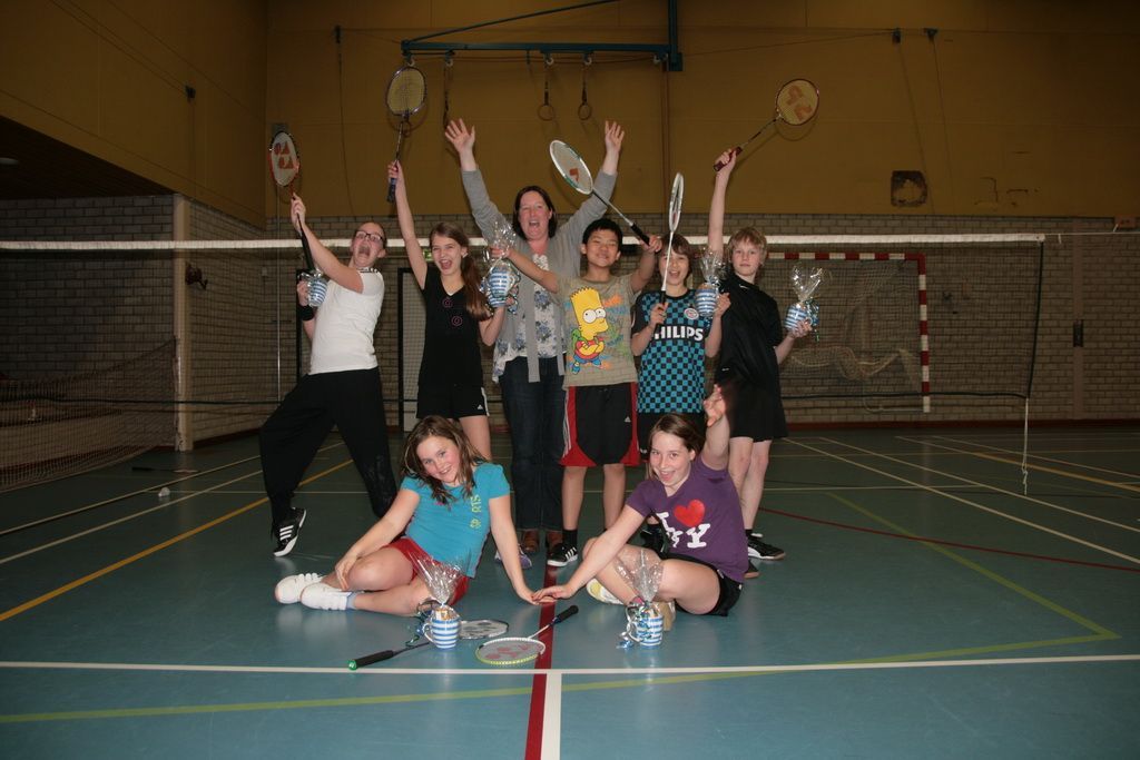 Een groep mensen staat en zit in een gymzaal, met badmintonrackets in de hand, en ze juichen.