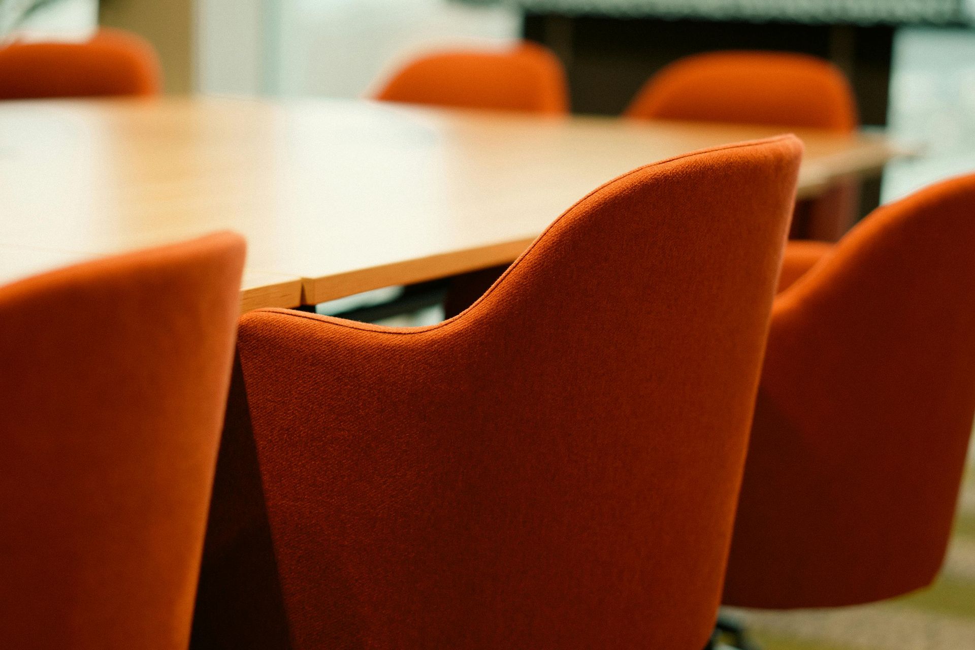 Een perspectiefopname van oranje stoffen bureaustoelen die rond een houten vergadertafel zijn opgesteld.