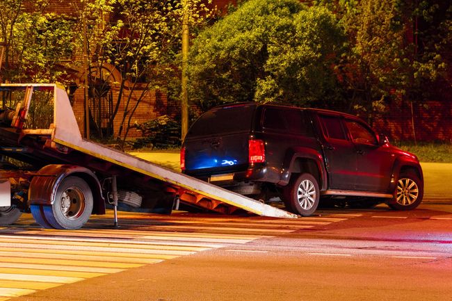 Flatbed tow truck securing a black SUV for nighttime emergency towing. Flatbed tow truck securing a black SUV for nighttime emergency towing.